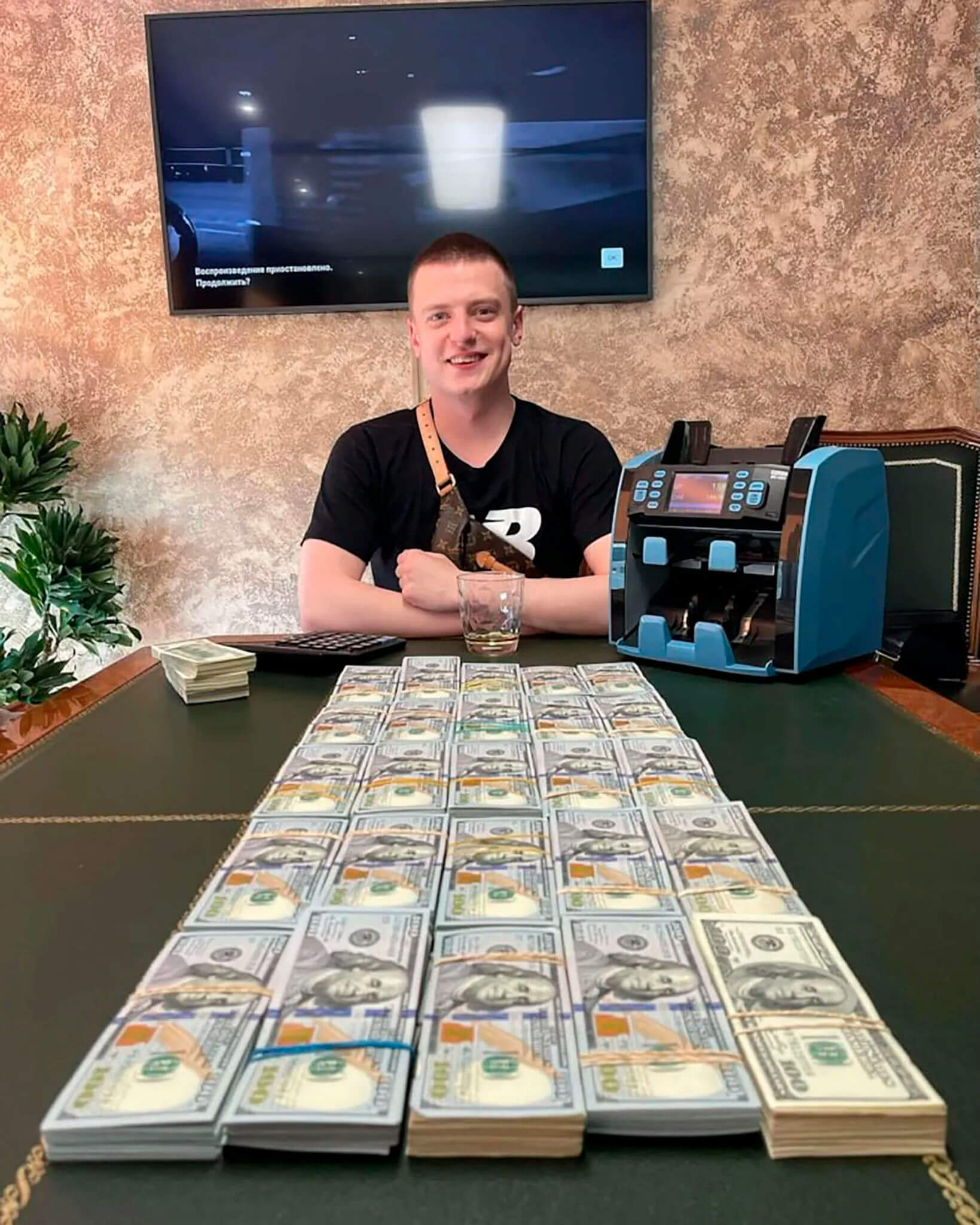 people-One young man smiling-A-stack of US hundred-dollar bills-B-money counting machine-C-glass with amber liquid