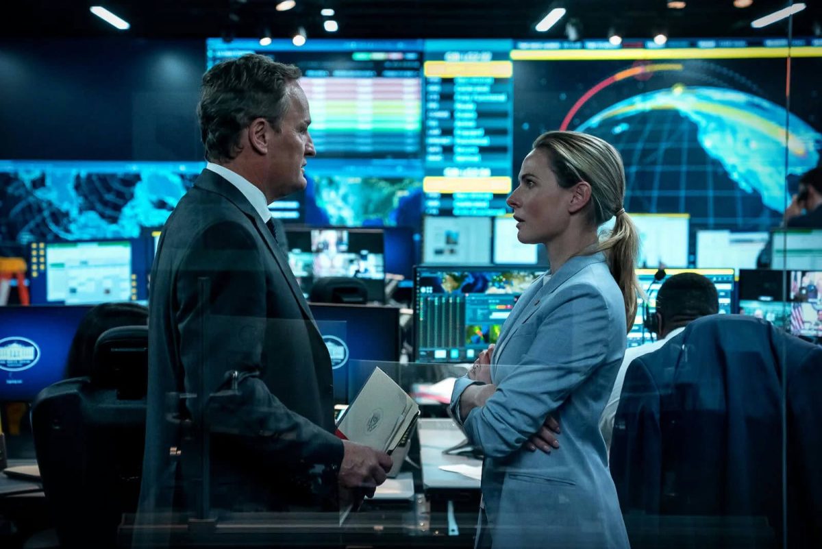 people-man in dark suit and white shirt-A-woman in light blue blazer-A-intense discussion-B-control room setting with monitors-C