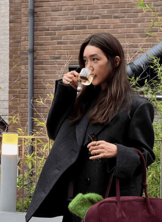 people-Woman-drinking tea-Medium shot-Oversized blazer-Holding glasses-Burgundy bag-Outdoor setting