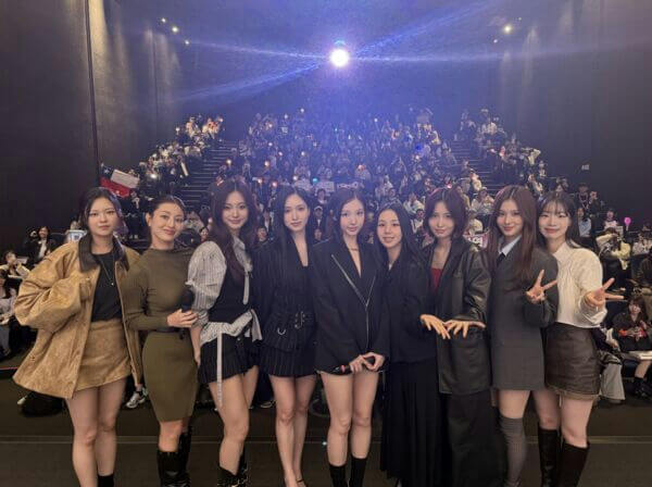 people-9 women-A-K-pop group-A-stage setting-A-audience in background-A-dark lighting-A-casual yet stylish outfits-A-peace signs visible