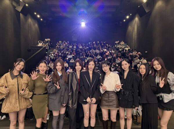 people-9 members of TWICE-A-K-pop group-A-standing on a stage-A-in front of an audience-B-in a dark theater or cinema setting-C