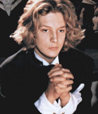 people-Young man-Blonde, wavy hair-Formal wear-Black suit jacket-White shirt cuffs-Hands clasped-Intense gaze