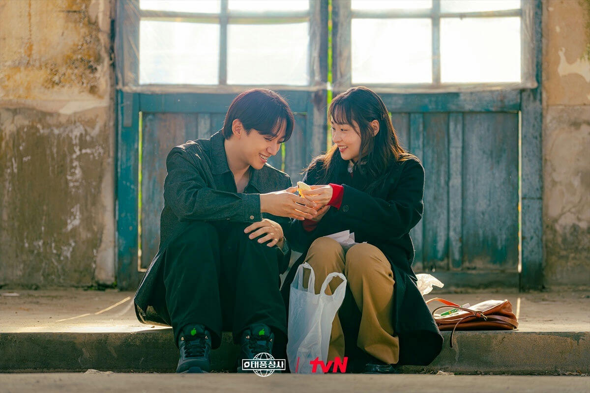 people-two young adults-A-sharing food-A-smiling-A-sitting outdoors-B-Korean drama promotional image-C-worn background-C