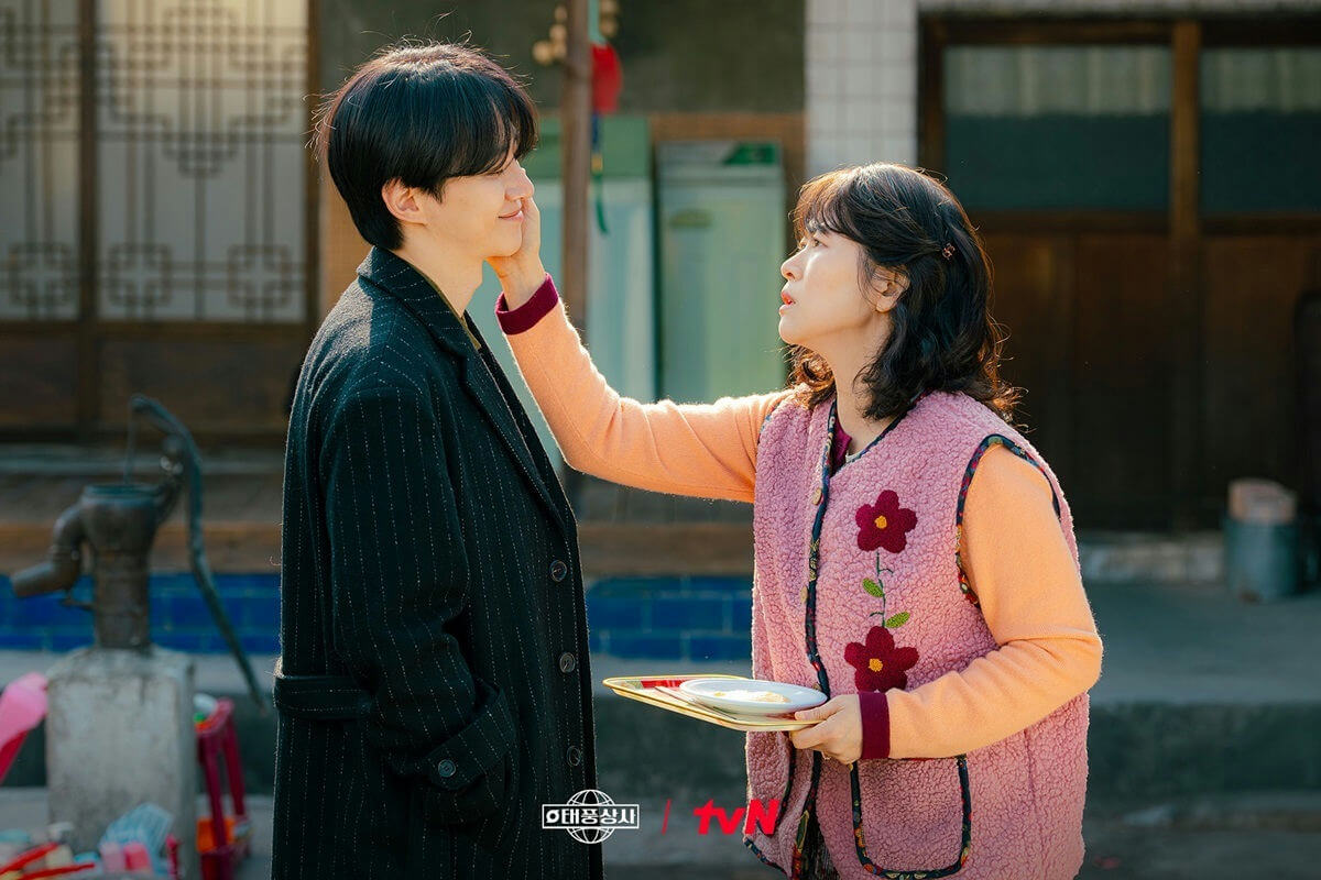 people-young man-gentle smile-motherly woman-affectionate touch-Korean drama setting-outdoor scene