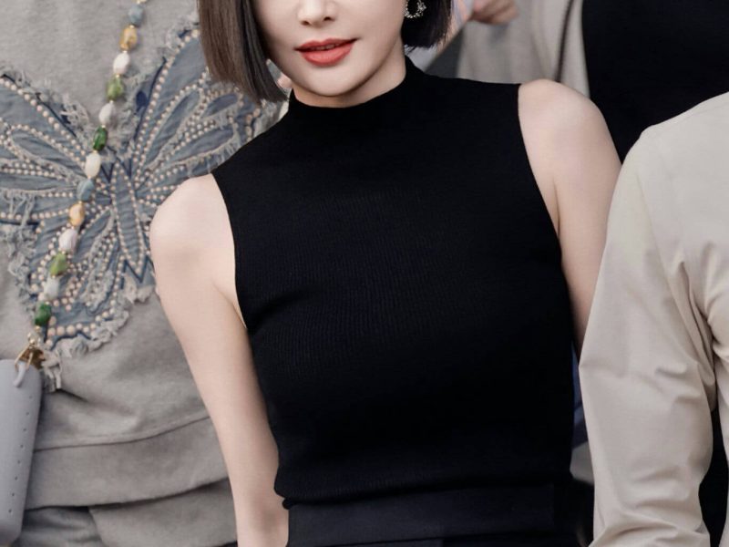 people-woman in black top-A-short black hair-A-looking at camera-A-outdoor setting-A-casual crowd background-A-jewelry earrings-A-formal pants-A-red lipstick-A-fashionable-A-celebrity-A