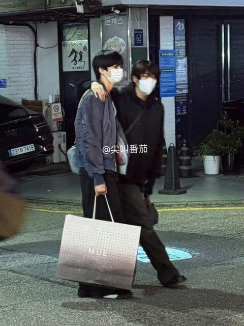 people-two men-A-walking on street-A-wearing face masks-B-one holding large shopping bag-C-arm around shoulder