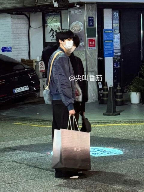 people-two individuals-A-wearing face masks-A-carrying shopping bags-A-standing on street at night-A-Korean storefronts visible in background