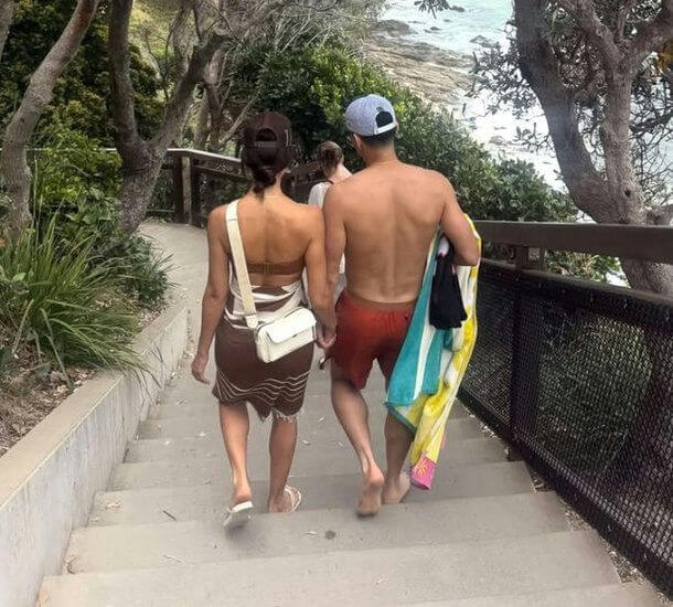 people-two people walking down stairs-beach bound-hand in hand-carrying towels-outdoor setting