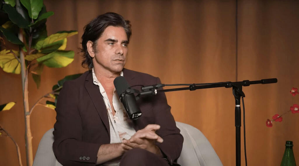people-John Stamos-sitting-microphone-interview-dark suit-indoor setting