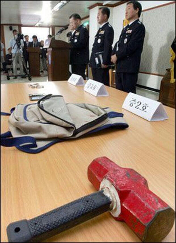 people-Three men in dark uniforms standing behind a podium and a table-A-Sledgehammer on a wooden table-B-Backpack on the wooden table-C-Signs with Korean characters on the table