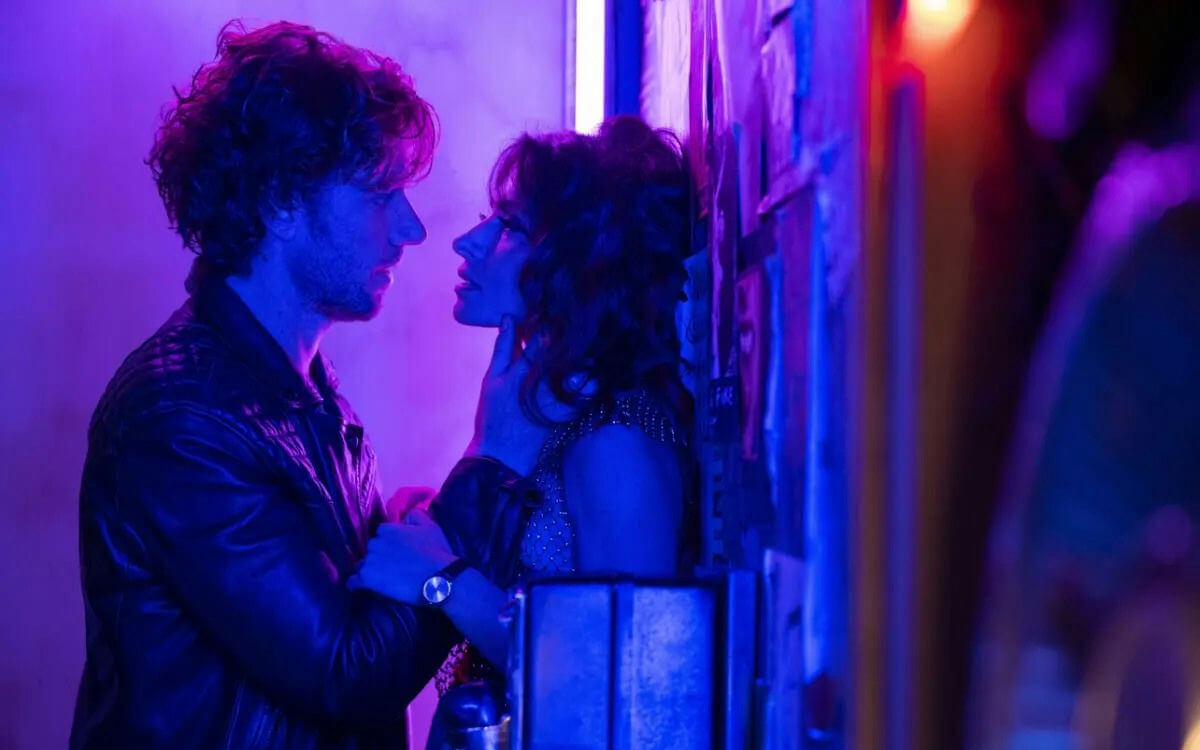 people-two individuals-A-intense gaze-A-neon lighting-A-intimate moment-B-man in leather jacket-B-woman leaning against wall-C-purple and blue glow