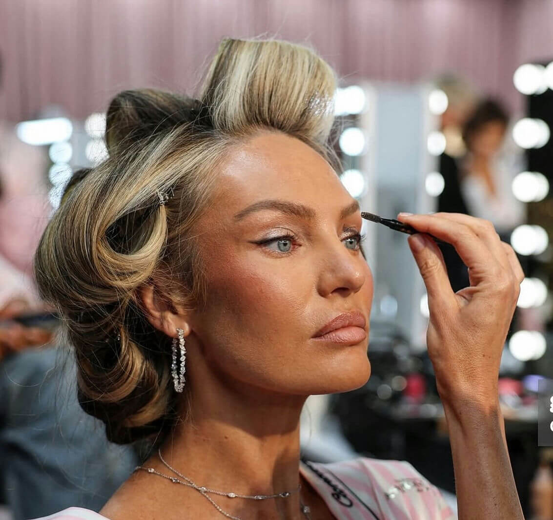 people-Candice Swanepoel-A-getting makeup applied-A-hair in rollers-B-diamond earrings-C-applying eyebrow product
