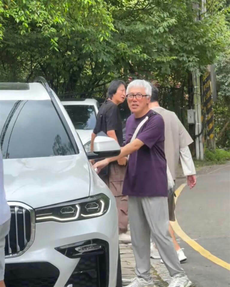 people-man with white hair and glasses-A-purple t-shirt-A-white SUV-A-outdoors-B-other people-B-trees and foliage-C