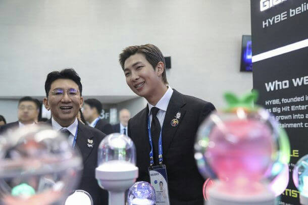 people-RM (BTS)-A-suit-A-Man in glasses-B-HYBE logo/display-C-light sticks (ARMY Bomb)
