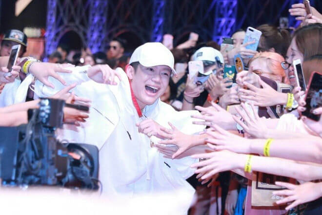 people-man in white outfit and cap-A-smiling widely-A-reaching towards crowd-B-fans reaching out-C-phones raised to take pictures
