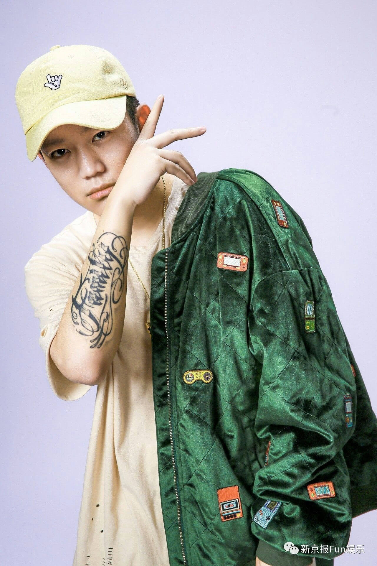 people-A-male subject-A-streetwear fashion-A-green quilted bomber jacket-A-arm tattoo-A-yellow baseball cap