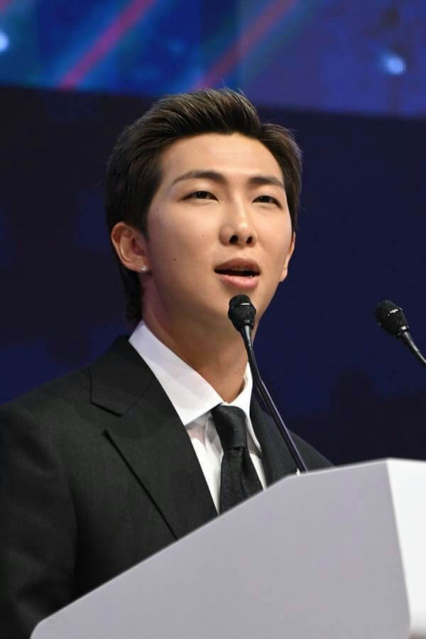 people-RM (Kim Namjoon)-speaking-at-a-podium-wearing-a-black-suit-and-tie