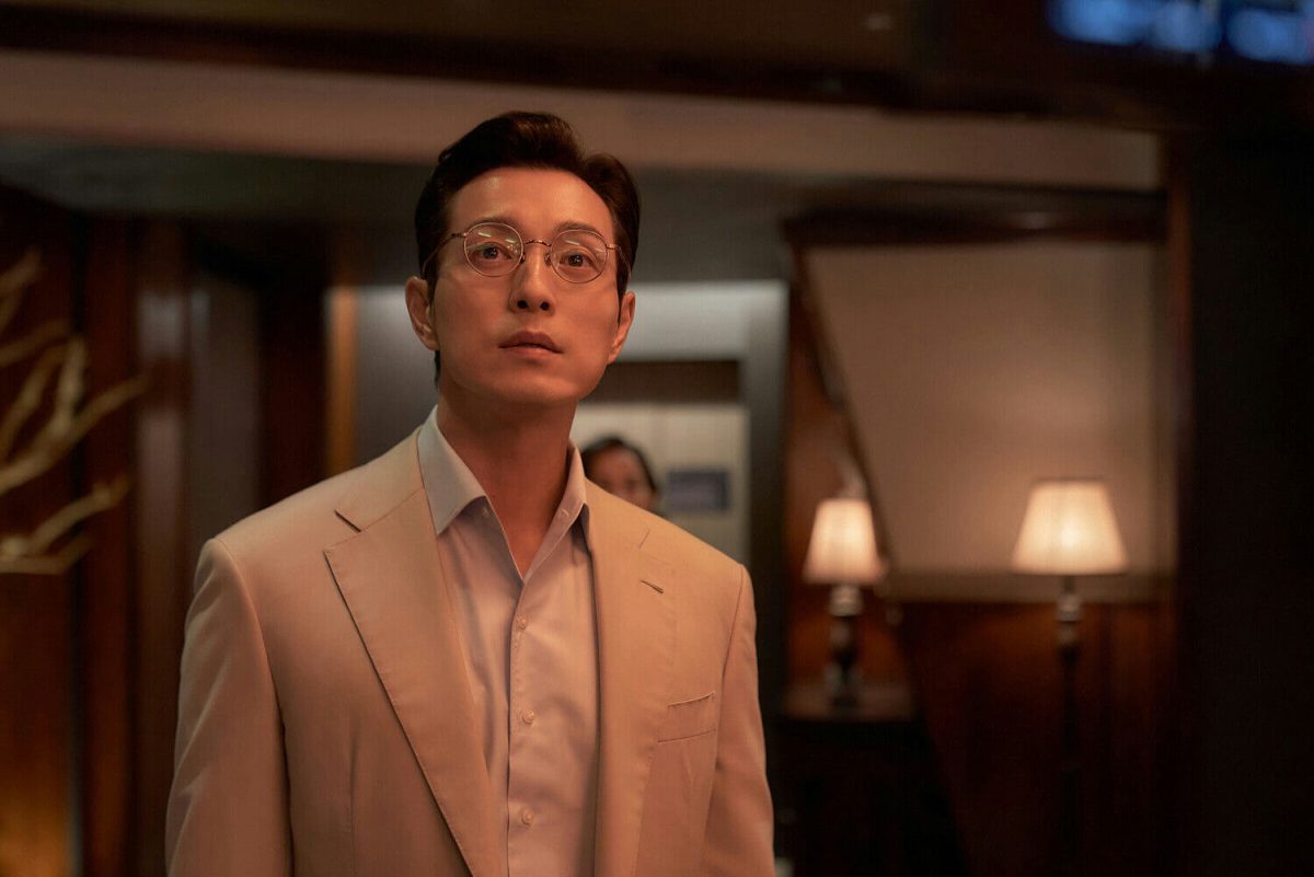 people-1-man-A-Asian-A-wearing-round-glasses-A-wearing-tan-suit-A-looking-up-B-interior-setting-B-dimly-lit-B-background-person-visible