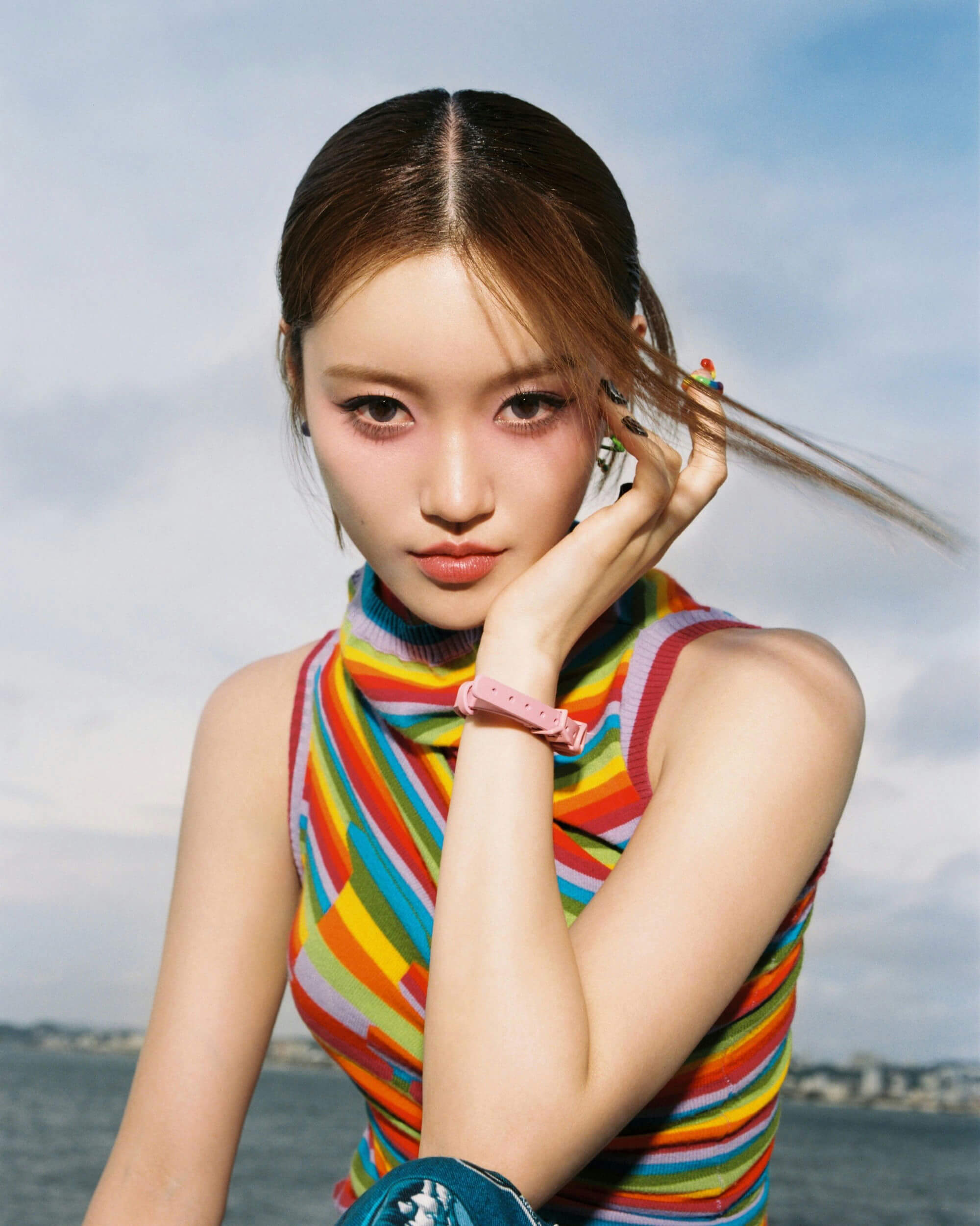 people-East Asian woman-A-colorful rainbow knit top-A-pink wristband-A-windblown hair-B-outdoor setting-C-blue and gray sky