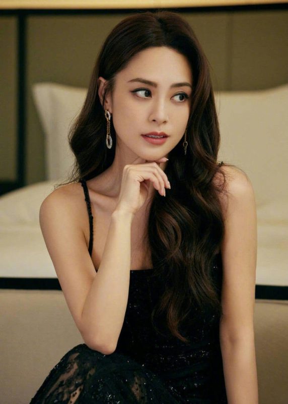 people-woman-long dark wavy hair-black sequined dress-diamond drop earrings-hand on chin-looking away