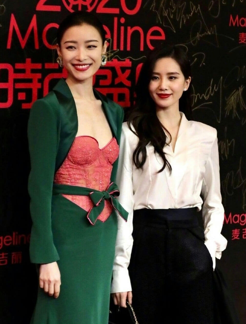 people-Two women-A-standing side-by-side-B-red carpet event background-C-formal attire
