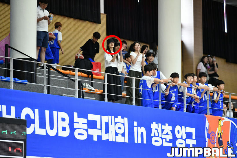 people-woman in black hat and white shirt clapping-A-basketball game spectators-A-young basketball players in blue jerseys-B-banner in Korean about a basketball tournament-C
