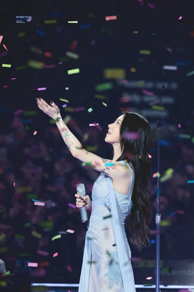 people-Female singer-A-long black hair-A-light blue dress-A-colorful tattoos on arm-A-confetti falling-A-holding microphone