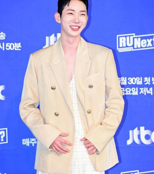 people-male celebrity-smiling-attire-beige double-breasted blazer-attire-white patterned garment-background-blue step-and-repeat backdrop