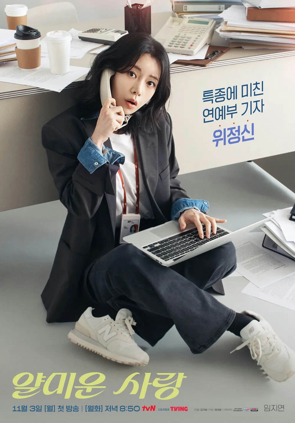 people-A-woman-A-sitting on floor-A-talking on phone-A-using laptop-B-Korean drama poster-B-entertainment reporter-B-cluttered desk-C-casual professional attire-C
