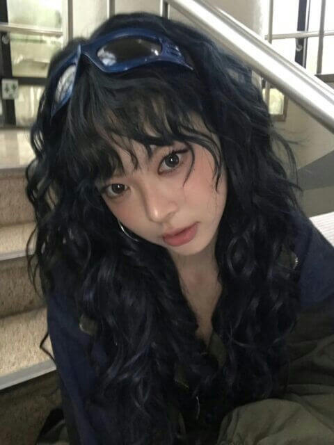 people-Asian female-A-long wavy dark hair-A-blue futuristic goggles on head-B-heavy eyeliner-B-subtle pink blush-C-khaki and dark blue clothing