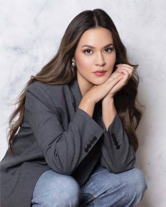 people-woman-squatting-gray blazer-jeans-long wavy hair-pearl earrings