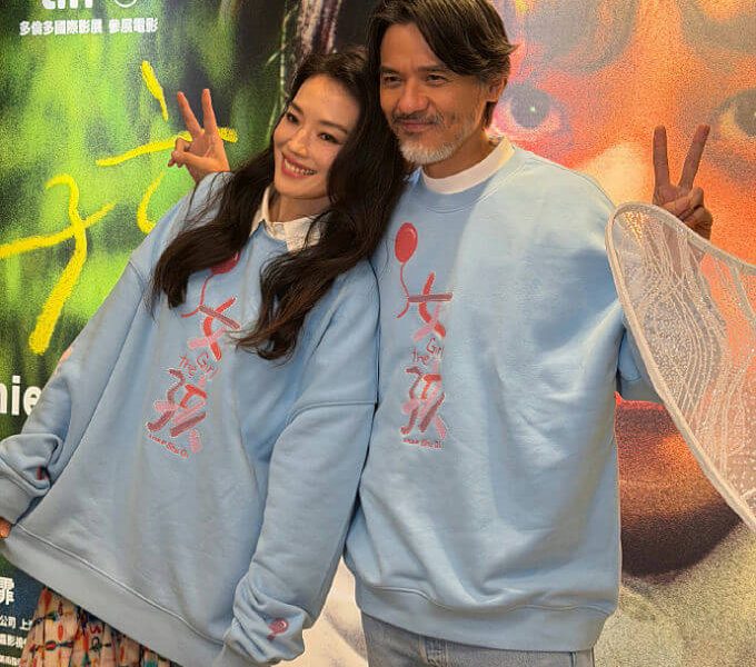 people-woman and man-smiling-posing-matching light blue sweatshirts-peace signs-film festival backdrop