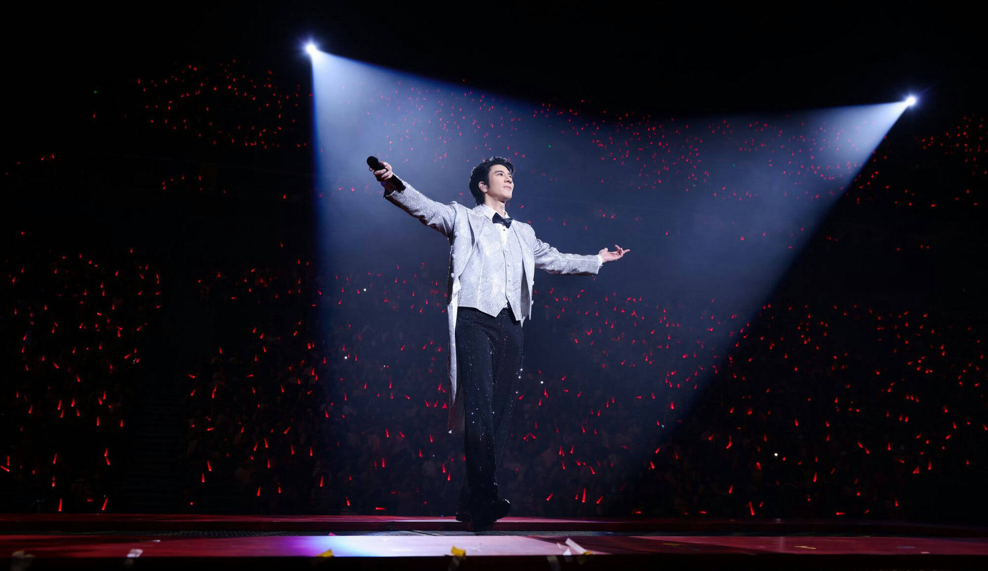 people-1-male singer-A-on stage-A-holding microphone-A-sparkling suit-A-spotlight-A-audience with light sticks-A-red lights-A-concert-A-performance