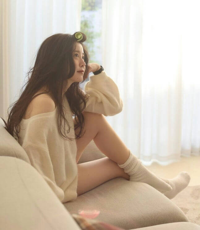 people-woman-A-sitting on a couch-A-wearing an off-the-shoulder white sweater-B-with a hair roller in her hair-C-wearing long white socks