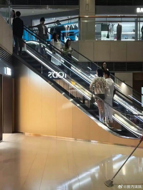 people-several people on an escalator-escalator-shopping mall interior-cleaner mopping floor-signage reading "2001"
