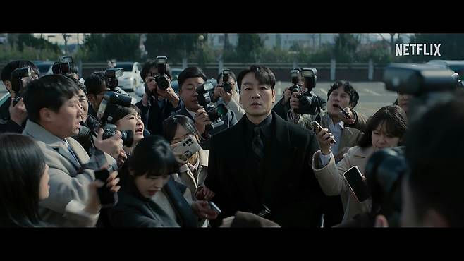 people-A-man in black suit-A-crowd of reporters-B-flashing cameras-C-Netflix logo