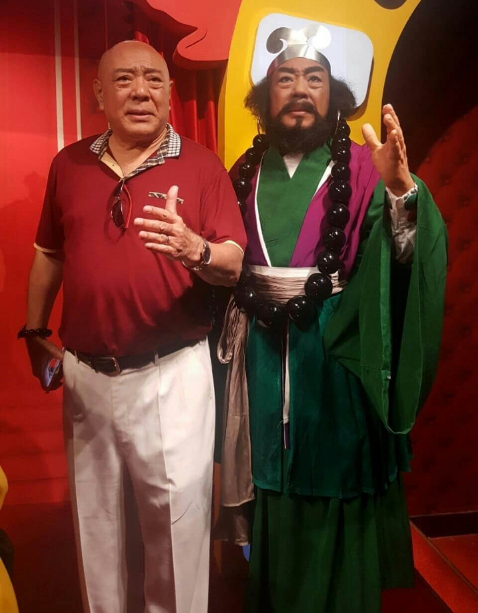 people-man in red shirt and white pants-wax figure of bearded historical/mythological character-posing indoors-museum or exhibition setting