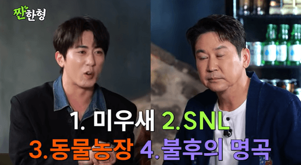 people-Man on the left (speaking)-Man on the right (listening intently)-Korean text overlays-TV show context