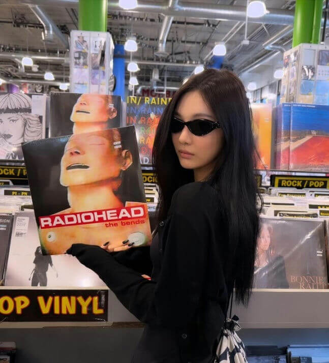 people-woman-A-holding-a-vinyl-record-B-wearing-sunglasses-C-in-a-record-store