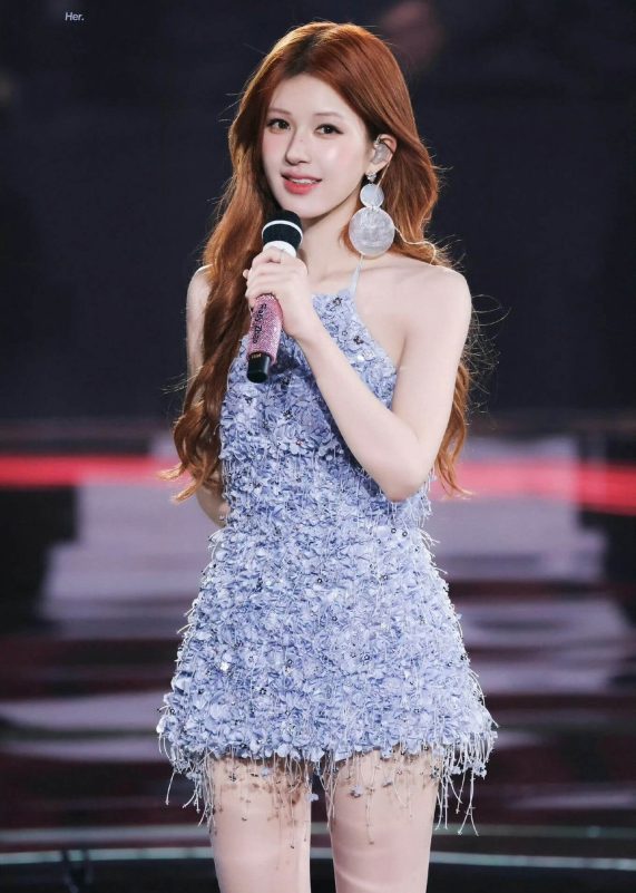 people-woman-holding microphone-performing-long reddish-brown hair-light blue textured mini dress-large circular earrings