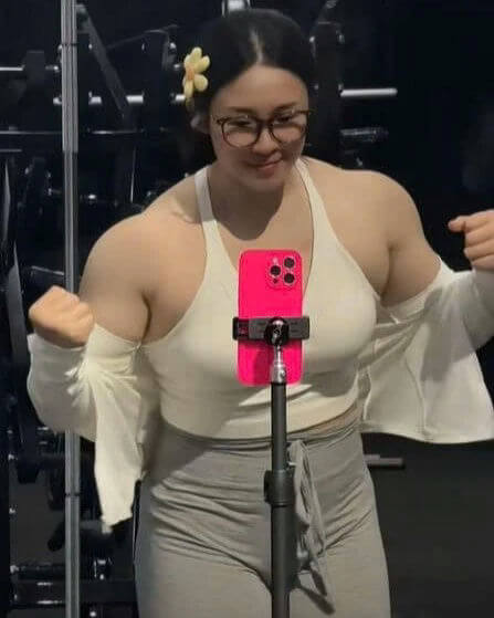 people-A-female bodybuilder-A-posing-A-gym-A-selfie-A-phone-A-athletic build-A-glasses-A-white top-A-yellow flower hair clip