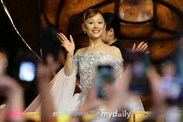 people-Ariana Grande-A-waving-A-smiling-A-off-the-shoulder-dress-B-crowd-C-event