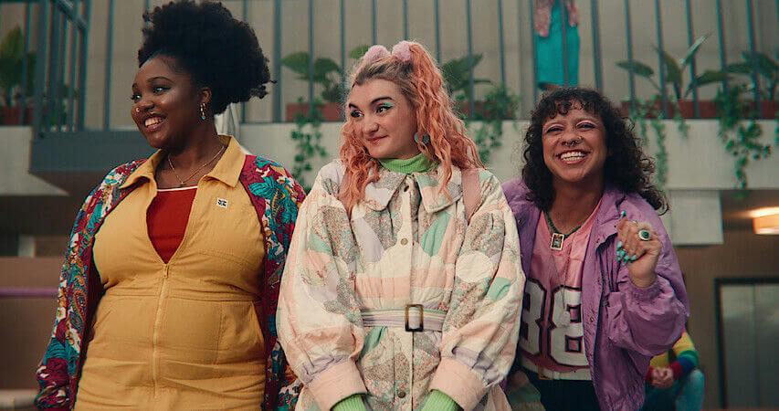 people-three women-A-colorful outfits-A-smiling-A-pink hair-B-quilted coat-B-yellow jumpsuit-C-purple jacket-C-curly hair