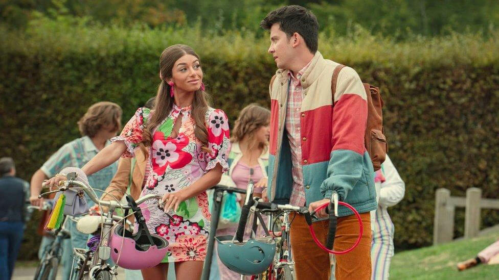 people-woman-in-floral-dress-A-man-in-color-block-jacket-A-bicycles-A-outdoor-setting-A-pink-helmet-A-brown-backpack-A