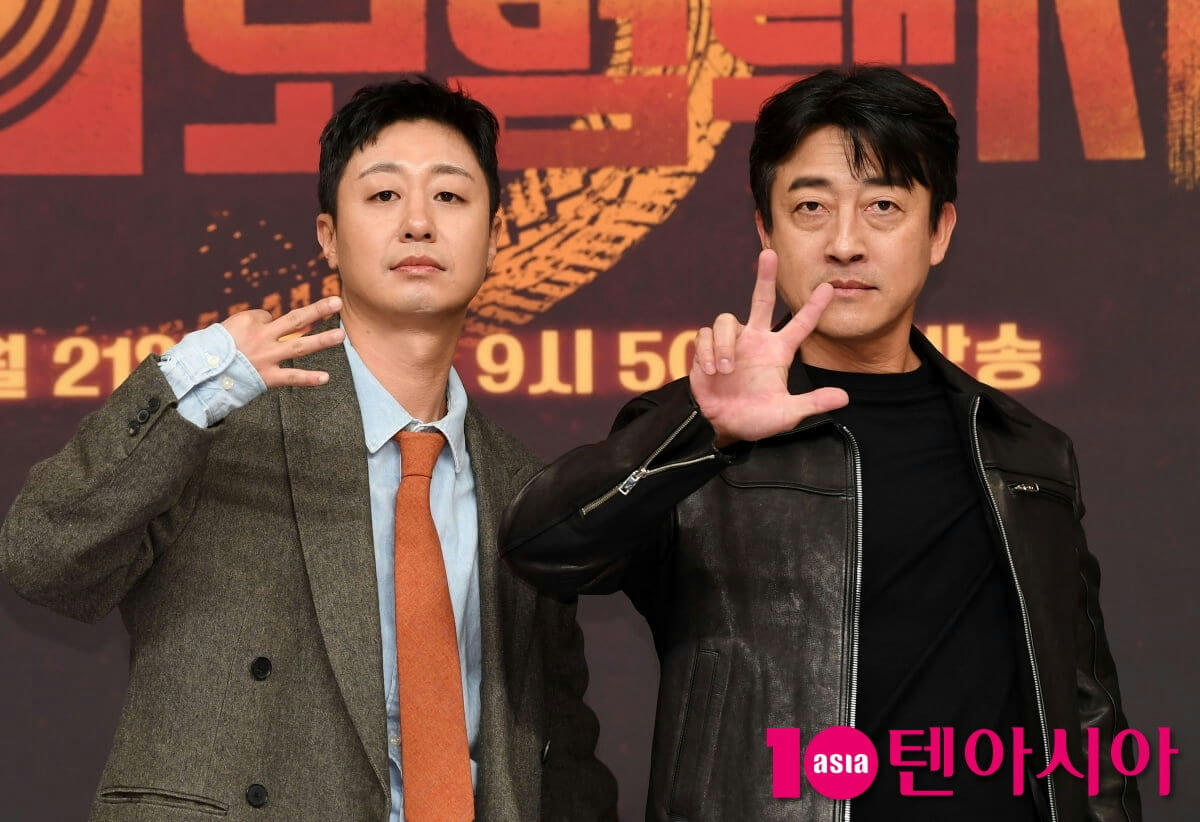 people-Two Korean men-A-posing for photo-B-making hand gestures-C-standing in front of backdrop