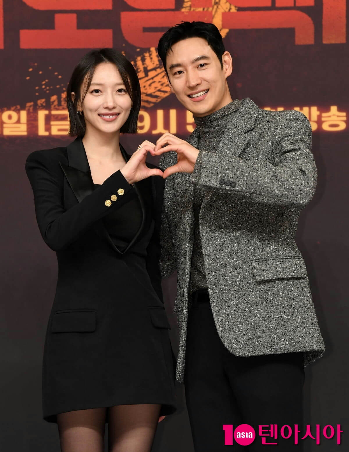 people-woman and man-posing for photo-making heart gesture-smiling-black dress-grey tweed blazer