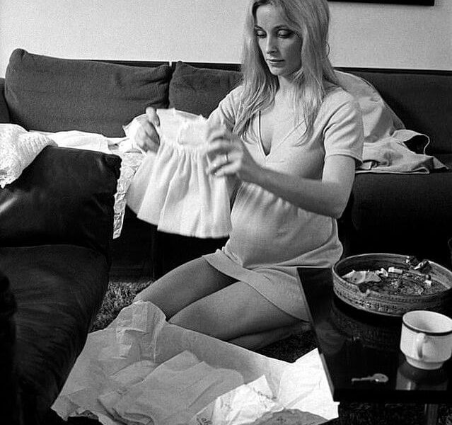 people-Sharon Tate-A-pregnant-A-kneeling-A-holding baby dress-B-unpacking gifts-B-casual wear-C-indoor setting-C