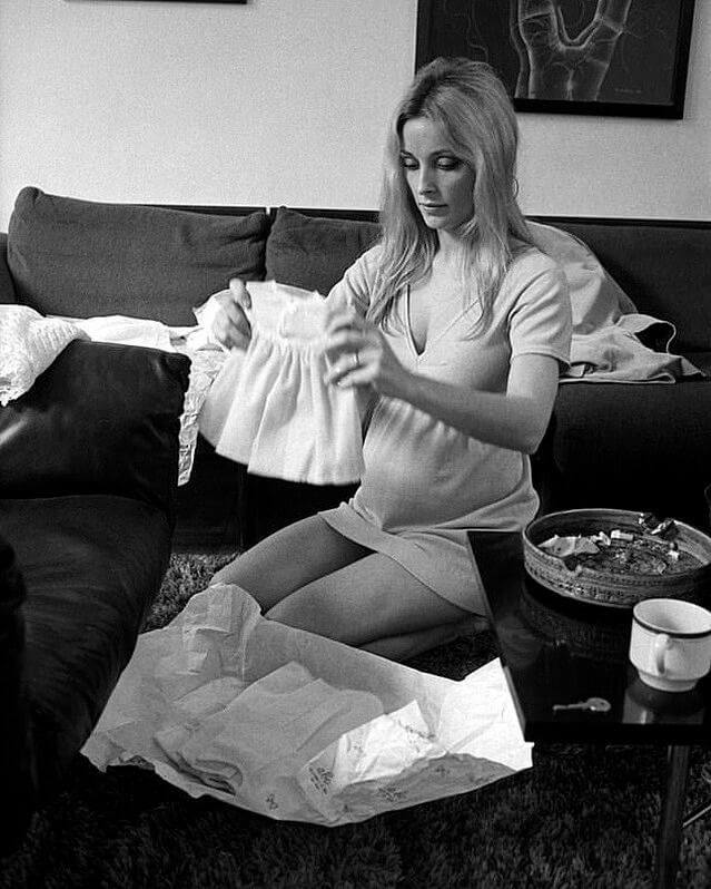 people-Sharon Tate-A-pregnant-A-kneeling-A-holding baby dress-B-unpacking gifts-B-casual wear-C-indoor setting-C