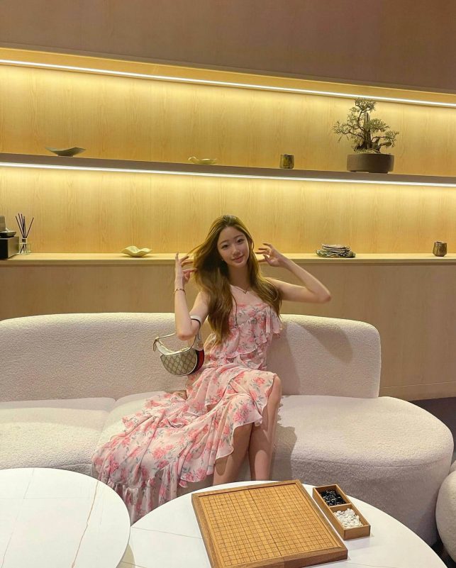 people-1-woman-A-sitting-A-pink floral dress-A-light wood shelves-A-textured white sofa