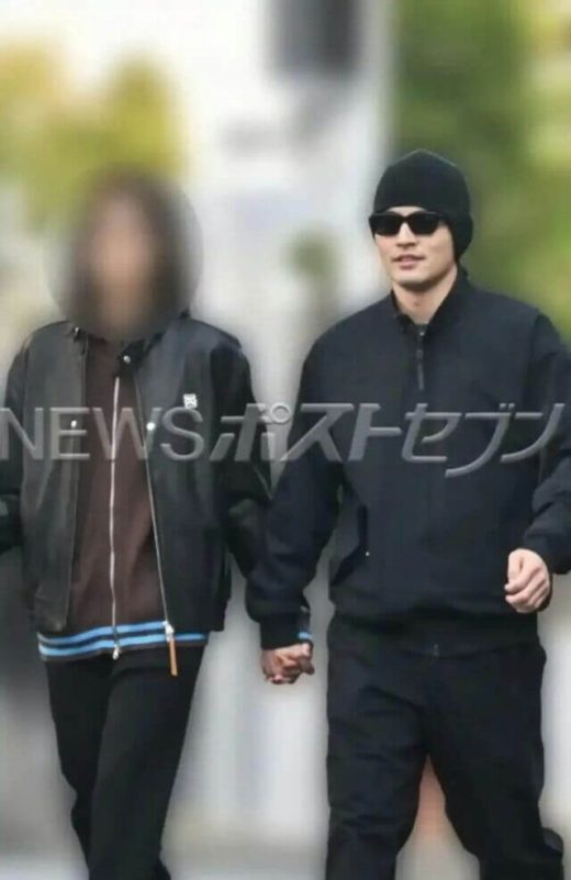 people-Two people walking outdoors-A-holding hands-A-man wearing a black beanie and sunglasses-B-woman with face blurred-C-Japanese text watermark